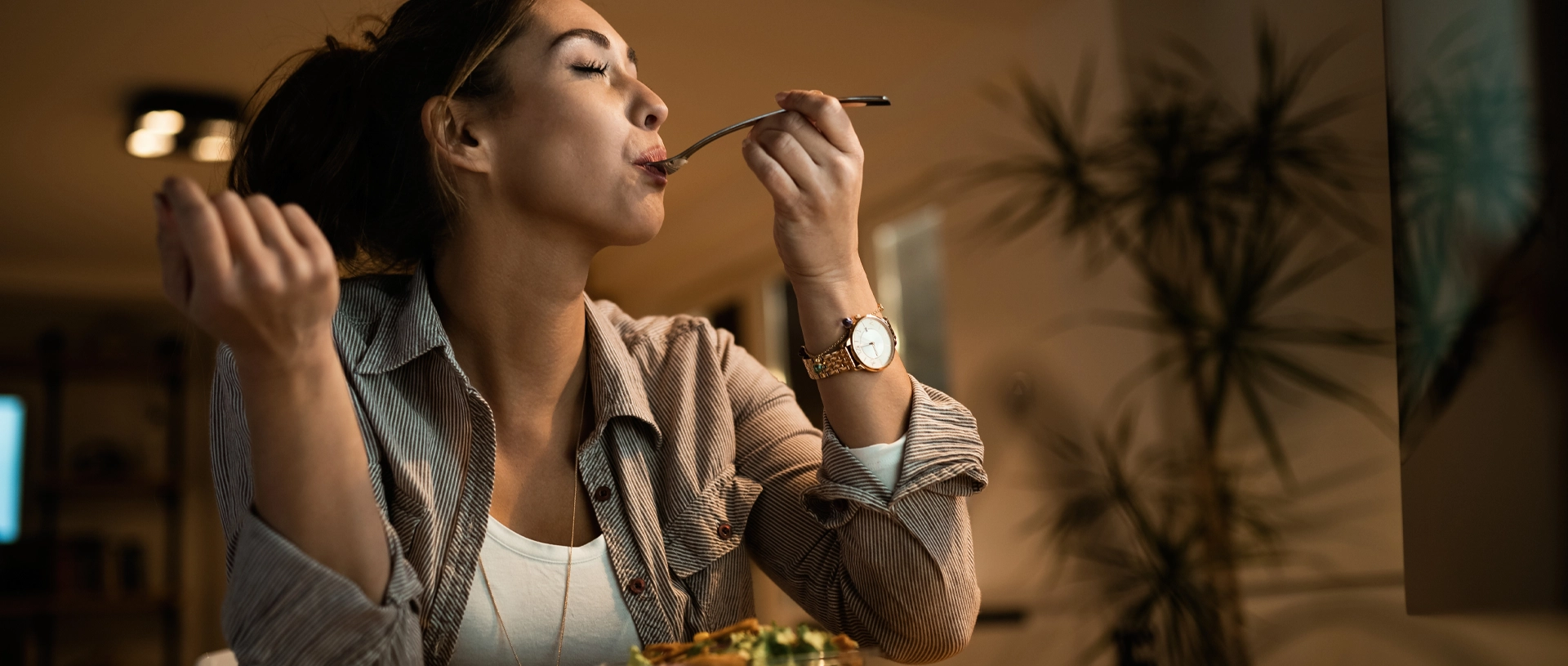 Femeie care mănâncă în timp ce lucrează seara, ilustrând relația dintre stres, alimentație și echilibrul emoțional