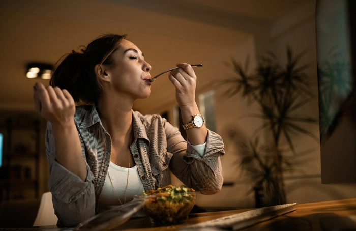 femeie care mănâncă în timp ce lucrează, ilustrând relația dintre stres emoțional, anxietate și alimentație